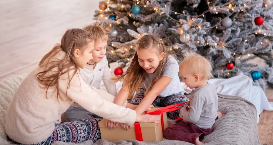 Siblings opening a gift in the family room beside a Christmas tree.